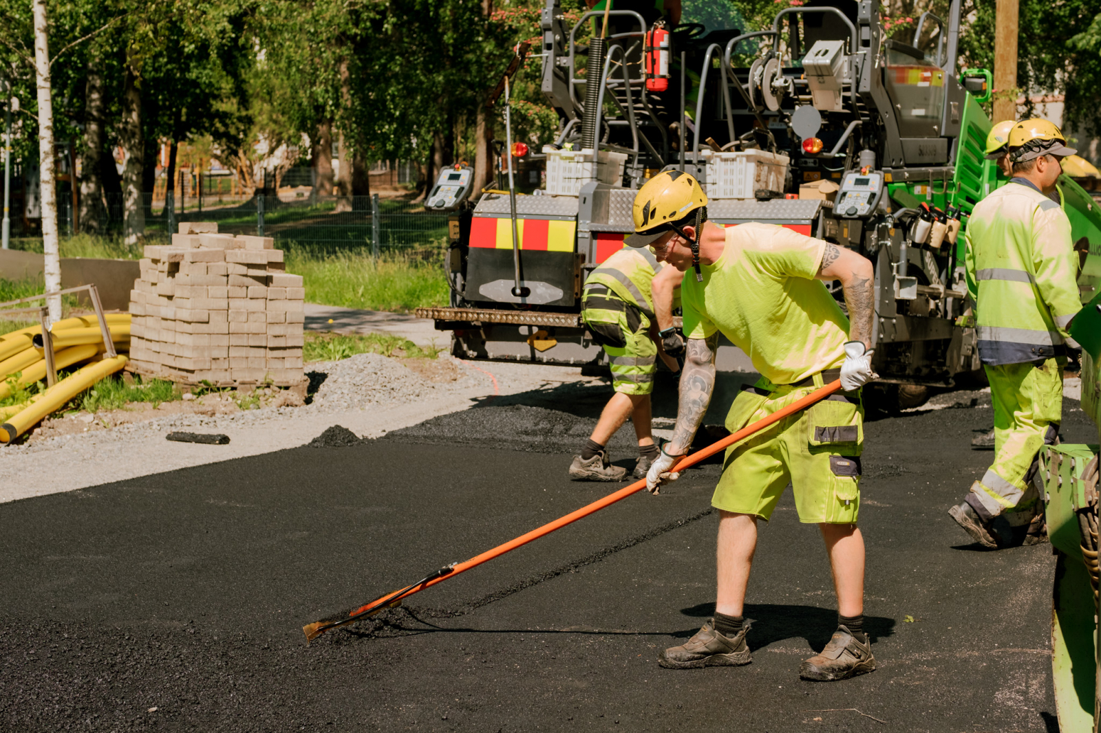 Asfalttityöntekijä tasoittaa levitettyä asfalttimassaa käsikolalla.